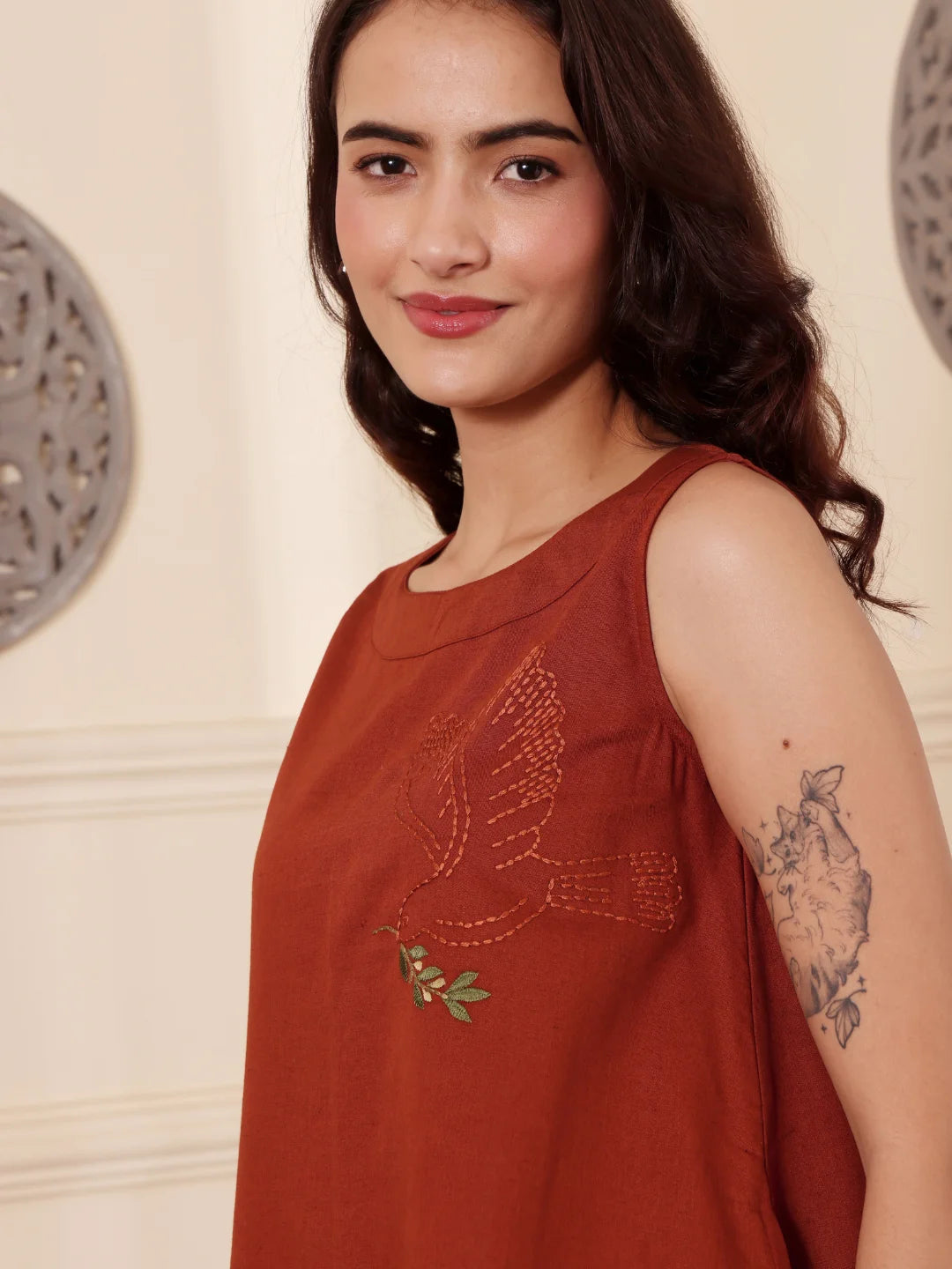 Left pose of a Woman wearing a rust color cotton linen dress with embroidery in an elegant interior