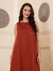 Front pose of a Woman wearing a rust color cotton linen dress with embroidery in an elegant interior