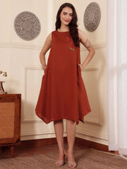 front pose of a Woman wearing a rust color cotton linen dress with embroidery and both hands in pocket in an elegant interior