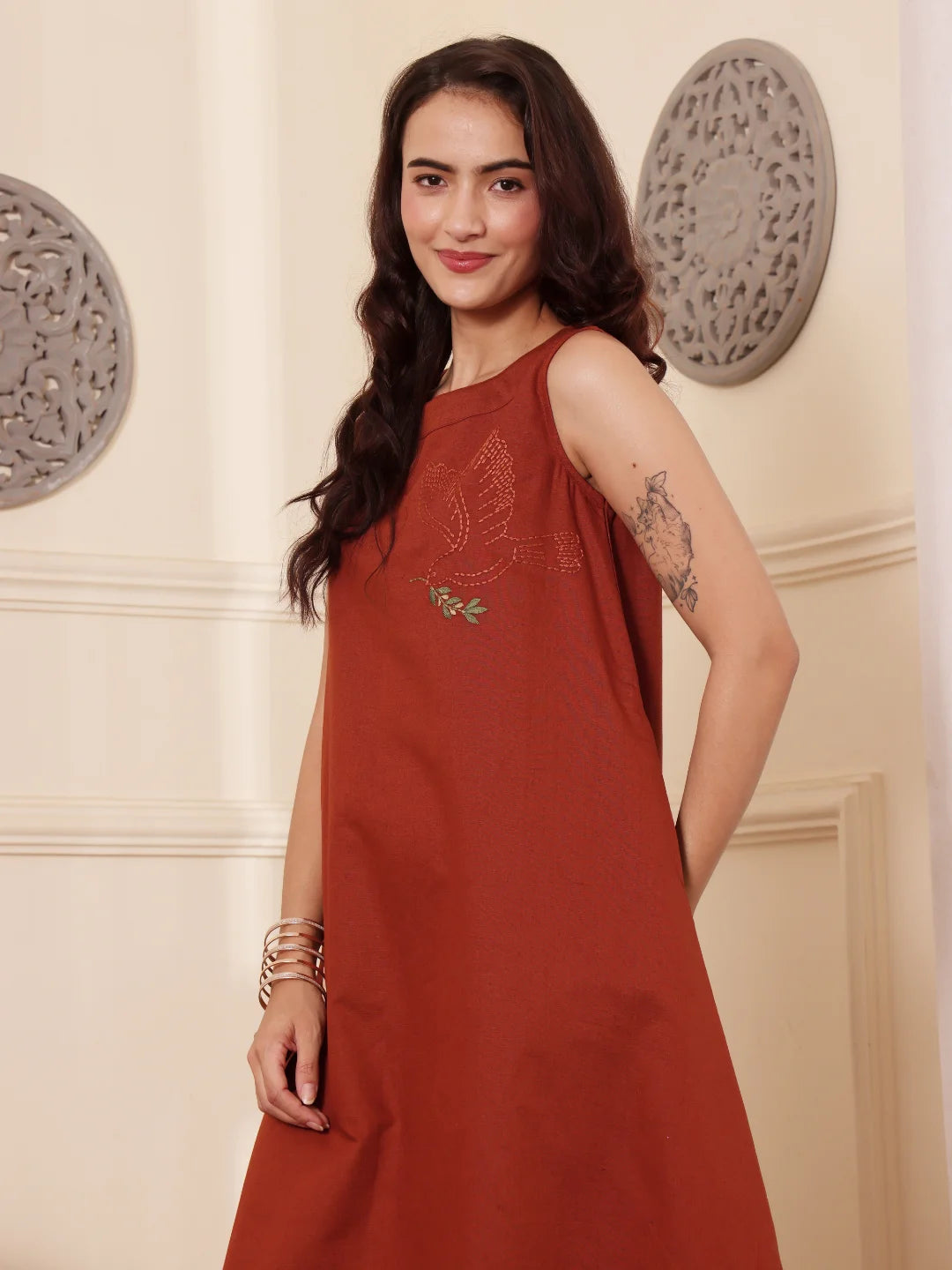 Left pose of a Woman wearing a rust color cotton linen dress with embroidery in an elegant interior setting