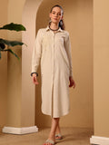 A woman models a long-sleeved, button-front linen midi dress in a warm cream or off-white color. The dress features a classic collar, long sleeves, and a relaxed, comfortable fit.