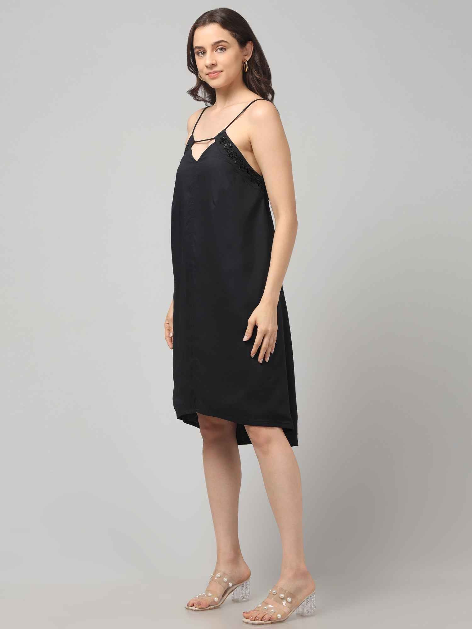 Side Profile of a women wearing a black resort wear cocktail dress with noodle strap and black embellishment on neckline