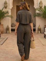 Back profile of a woman in a brown Co-ord Set - Half Sleeve crop Shirt and flared pants with pleats in front holding a woven bag.
