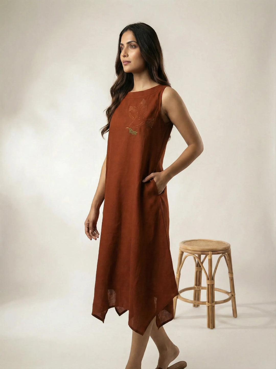Side profile of a women wearing a copper summer resort dress with bird embroidery and high low hemline