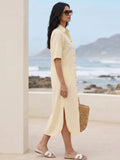 Side profile of a Woman in a cotton linen blend yellow shirt dress with embroidery holding a straw bag by a beach.