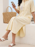 Woman in a cotton linen blend yellow shirt dress with embroidery sitting on the ledge by the beach