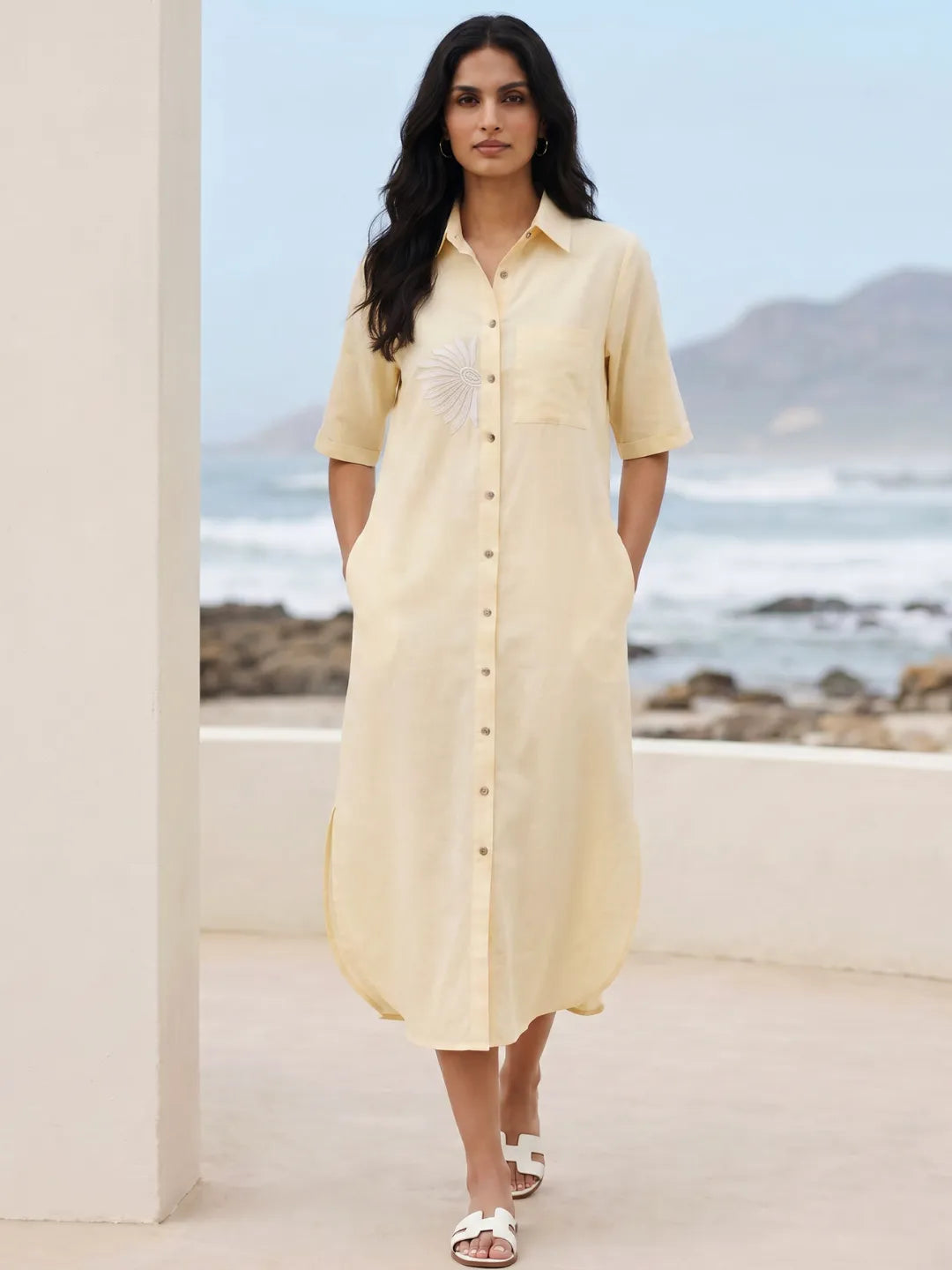 Woman in a cotton linen blend yellow shirt dress with embroidery walking with her hands in pocket.