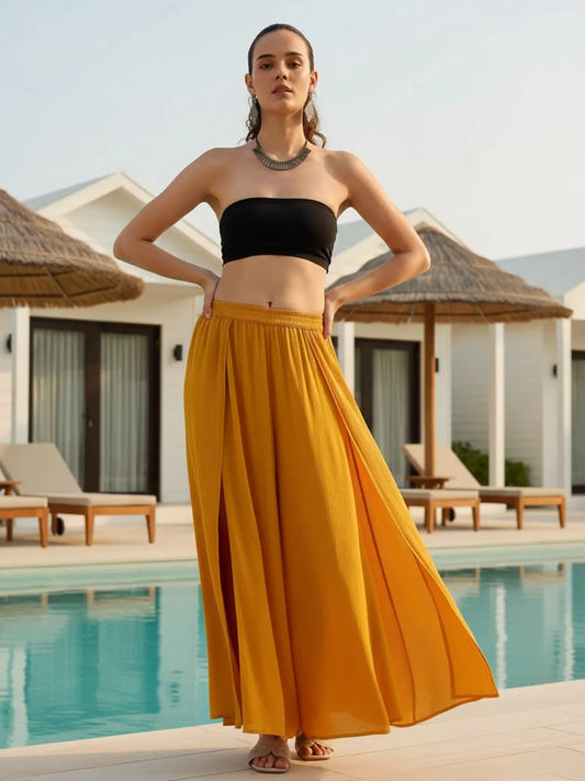 Woman in black top and yellow skirt standing by a pool with resort buildings in the background