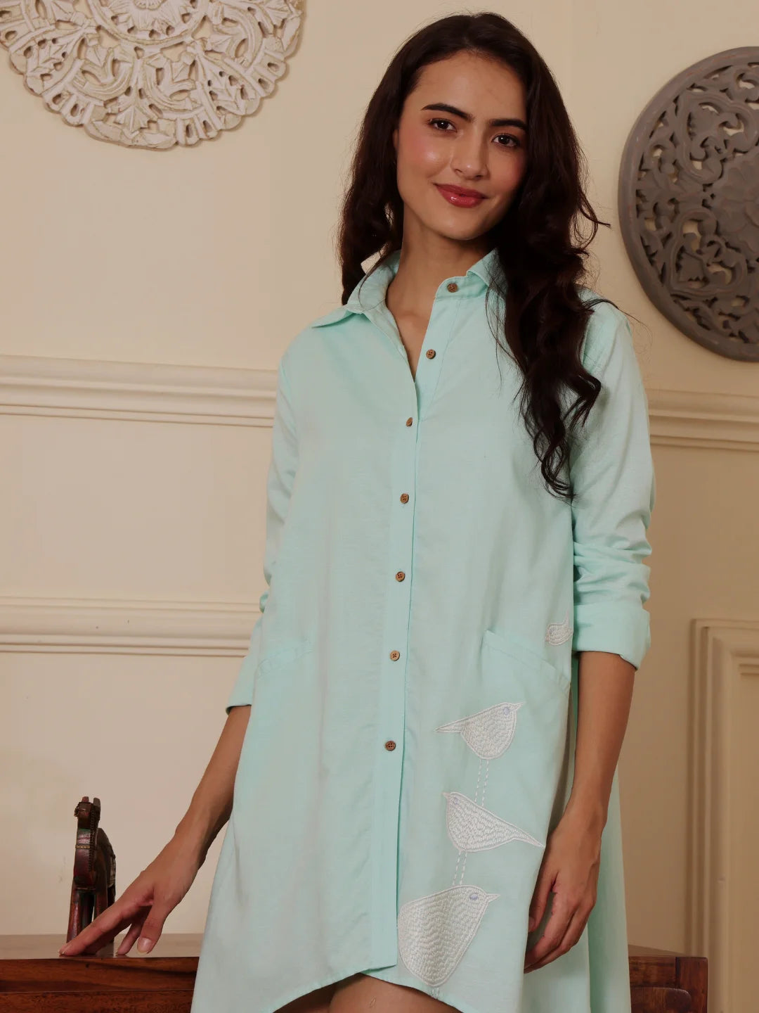 Woman wearing a mint blue linen blend Shirt dress with embroidery with a wooden table in the background