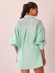 A woman shown from the back wearing an oversized long-sleeve shirt dress with a pale mint green and vertical stripe pattern on the lower body and a solid light sage green yoke across the shoulders and collar.
