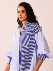 A woman wearing a light blue and navy striped button-up shirt with a solid light blue side panel, photographed against a plain light beige background.
