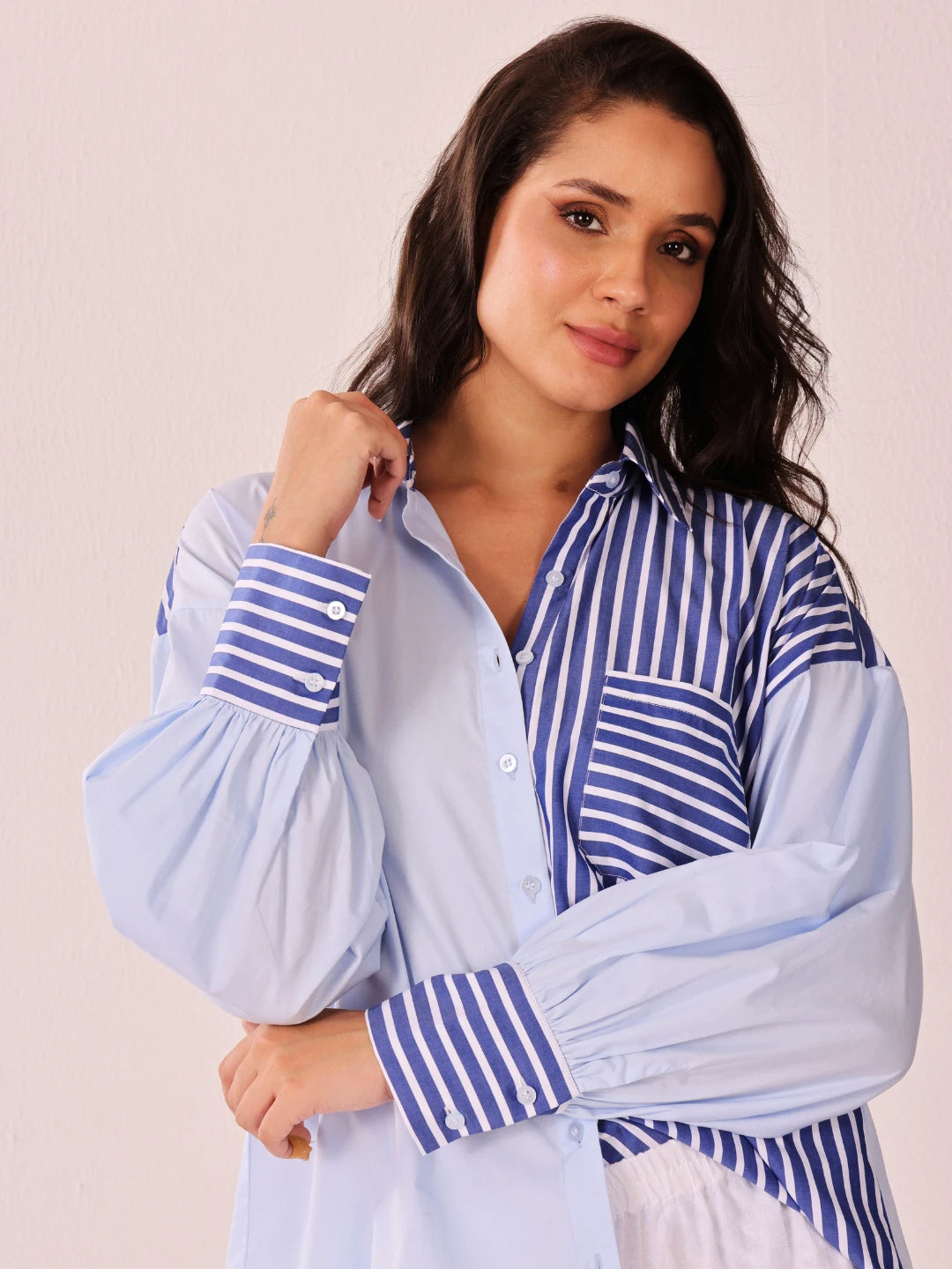 A woman modeling a light blue button-up shirt with blue and white vertical striped panels on the chest and cuffs, featuring dramatic balloon sleeves.