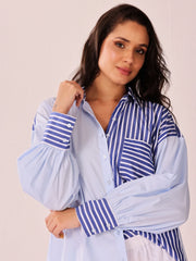 A woman modeling a light blue button-up shirt with blue and white vertical striped panels on the chest and cuffs, featuring dramatic balloon sleeves.