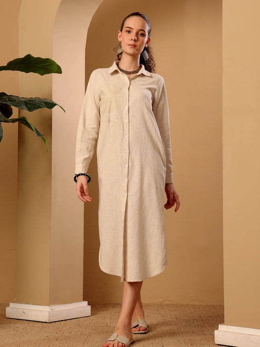 A woman models a long-sleeved, button-front linen midi dress in a warm cream or off-white color. The dress features a classic collar, long sleeves, and a relaxed, comfortable fit.