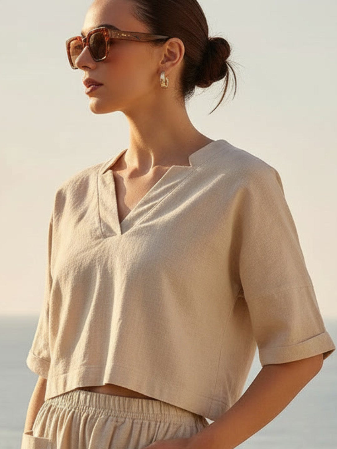 Woman wearing a beige co-ord set and sunglasses with a blurred background