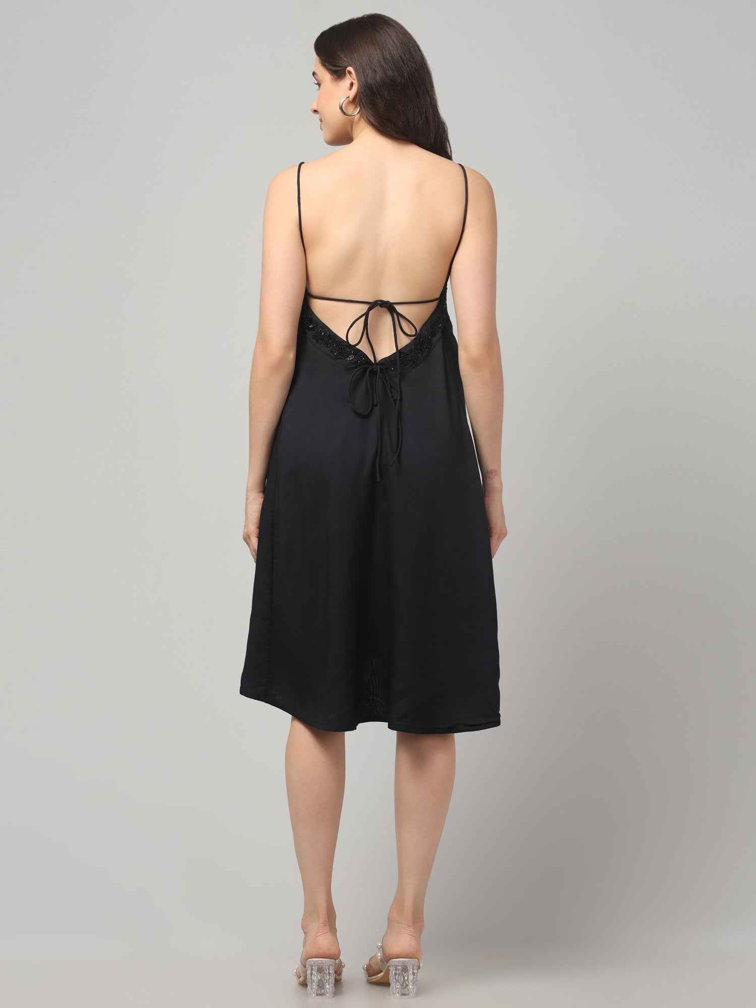 Women wearing a backless black resort wear cocktail dress with noodle strap and black embellishment on neckline