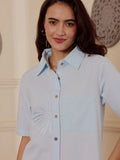 Woman wearing a light blue cotton embroidered linen shirt dress in an elegant room with decorative wall art.