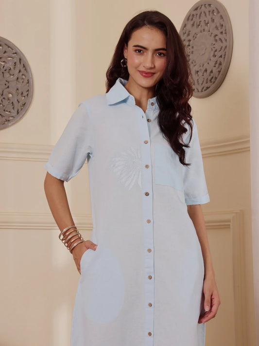 Close up shot of a Woman wearing a light blue cotton linen shirt dress in an elegant room with decorative wall art.