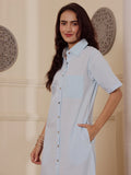 Side Profile of a Woman wearing a light blue cotton linen shirt dress in an elegant room with decorative wall art.