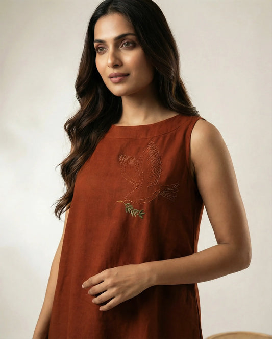Close up shot of a women wearing a copper color summer resort dress with bird embroidery.