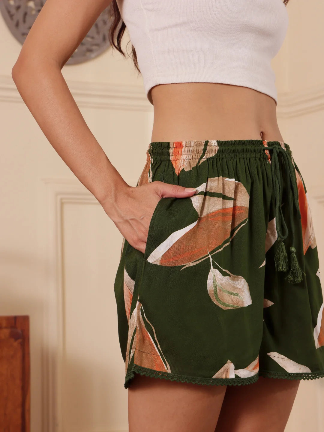 Right profile of a Women wearing a green floral-print shorts with drawcord and tassels with a white top against a neutral background