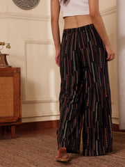 women back shot wearing a black boho print wide leg resort pants with white tank top in a room with textured wall