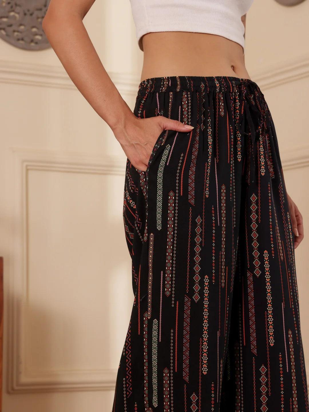 women closeup shot wearing a black boho print wide leg resort pants with white tank top in a room with textured wall
