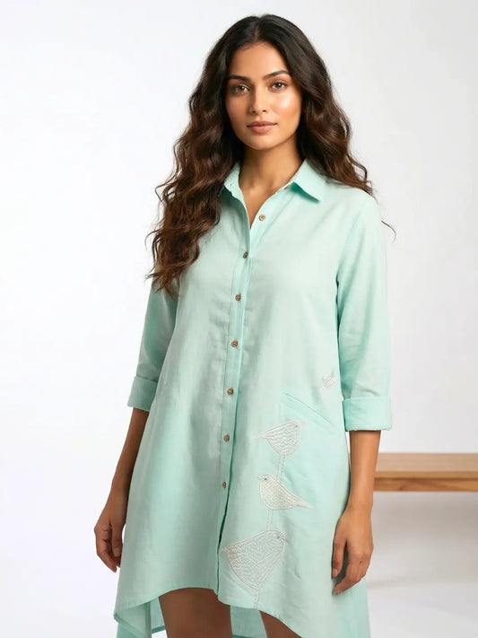 Women wearing a cotton Linen Mint color vacation Shirt dress with Birds embroidered and high low hemline.
