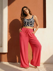 Woman wearing a black and white patterned top and pink pants against a warm-toned wall.