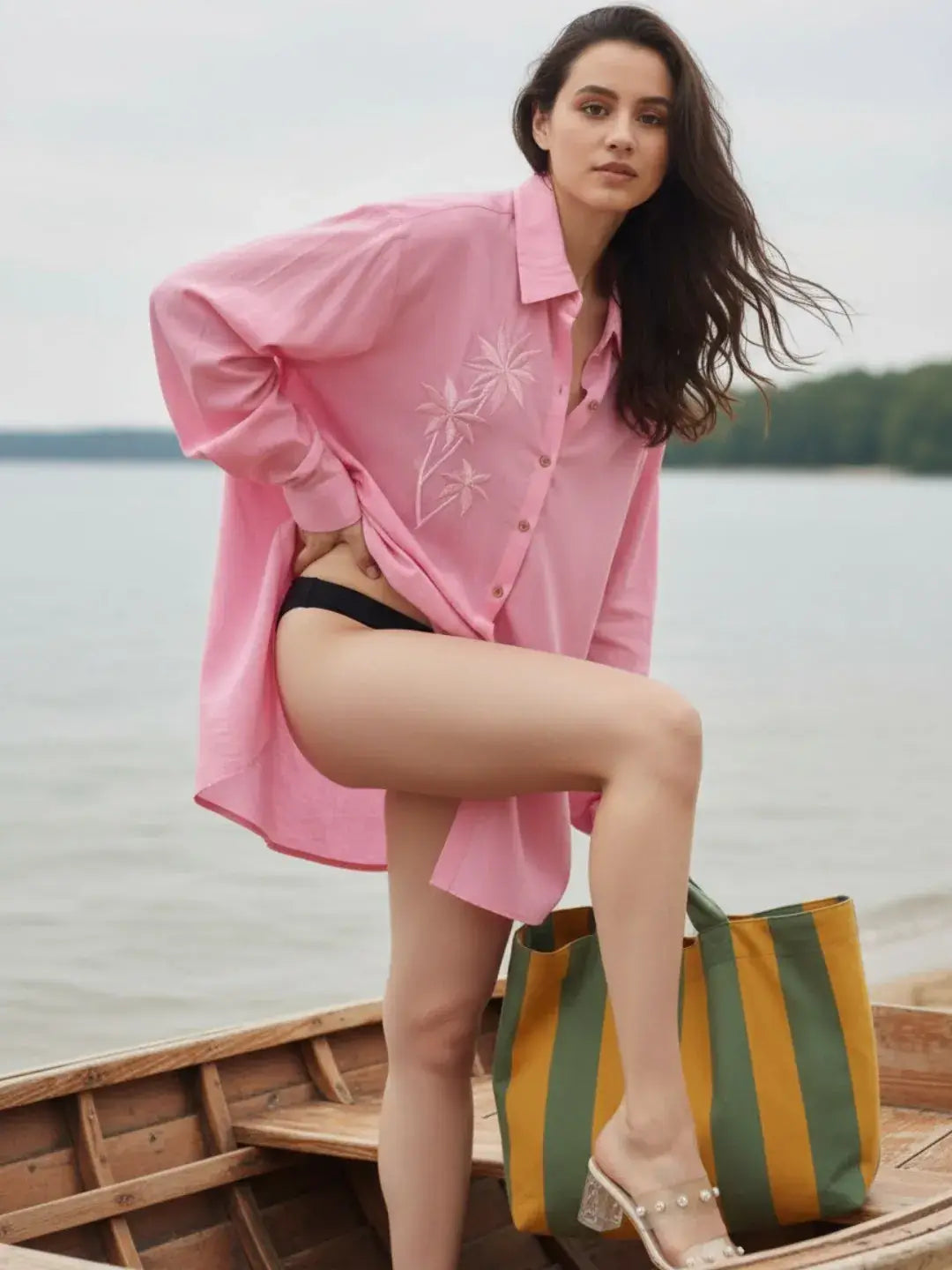 Woman in a pink shirt and black bikini sitting on a wooden dock by a lake.