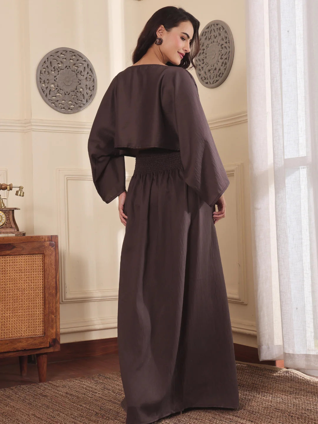Back pose of a Woman wearing a brown co-ord set with crop top and Skirt with Slit in a room with decorative elements.