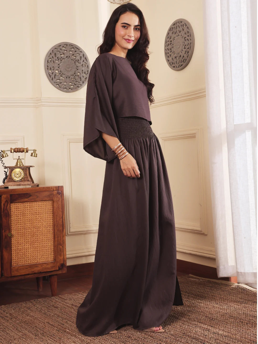Right pose of a Woman wearing a brown co-ord set with crop top and Skirt with Slit in a room with decorative elements.