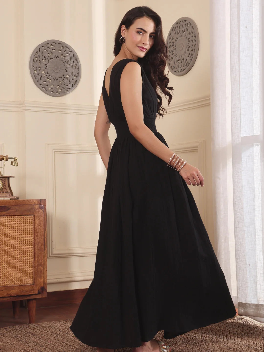 Woman in a black dress standing in a room with decorative wall patterns.