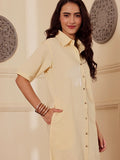 Side profile of a Woman wearing a light yellow cotton linen shirt dress with a floral design in a room with decorative elements.