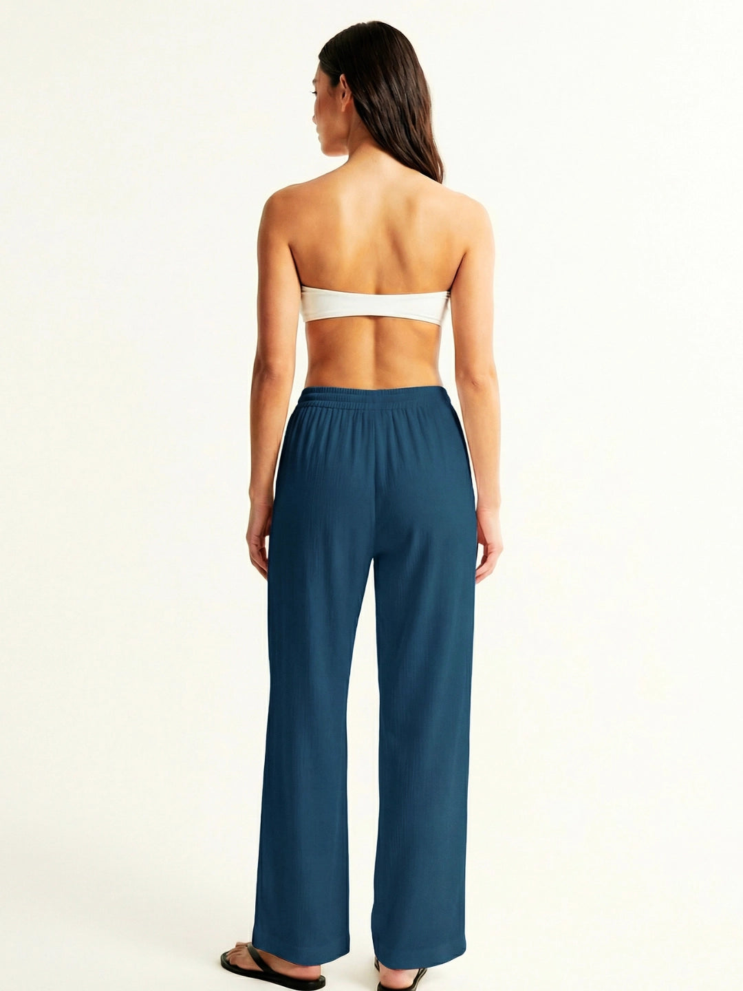 Woman wearing a strapless top and teal pants on a white background