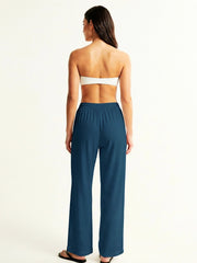 Woman wearing a strapless top and teal pants on a white background