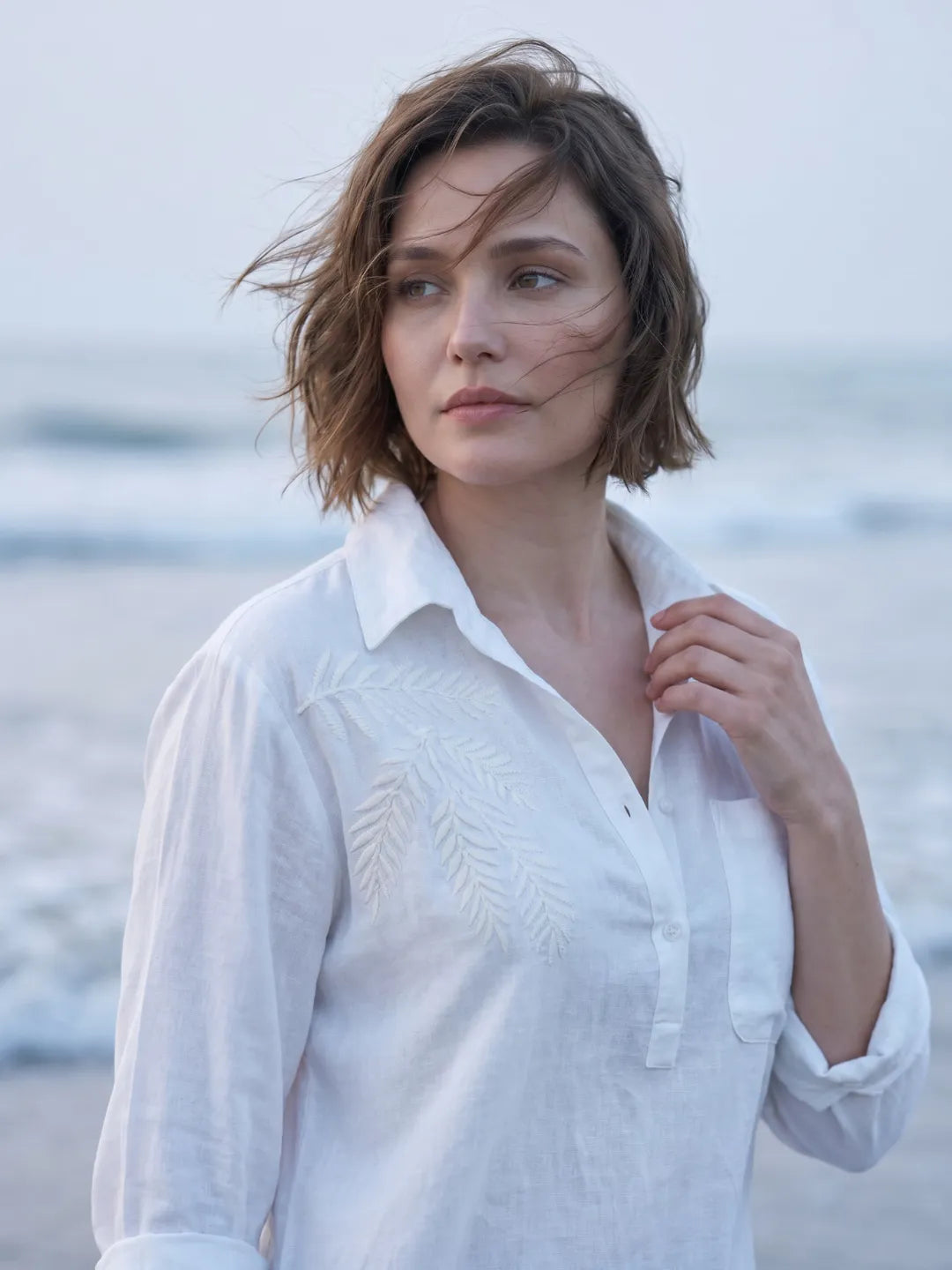 close up shot of a women wearing white linen blend beach shirt with embroidery and walking on the beach