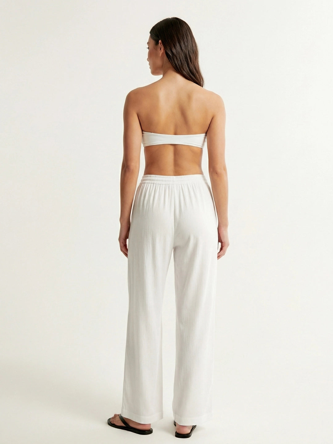 Woman wearing a white strapless top and wide-leg pants on a plain background