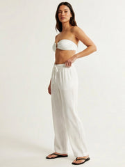 Woman wearing a white strapless top and wide-leg pants on a plain background
