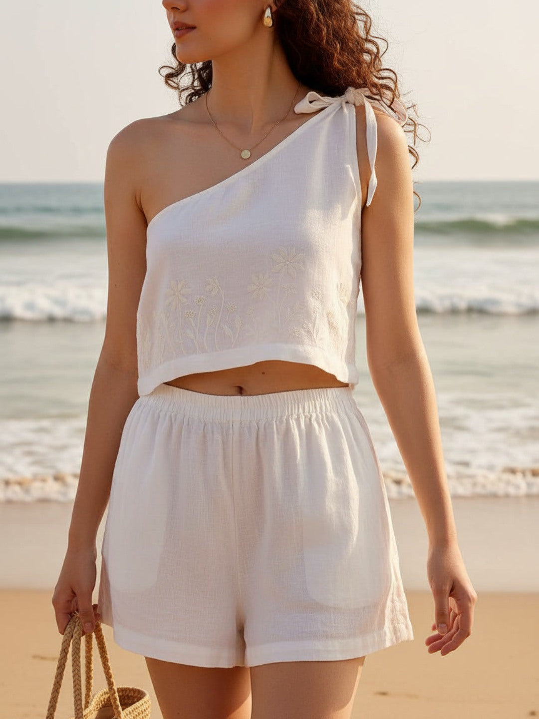 Woman in a white co-ord set standing on a beach with ocean waves in the background