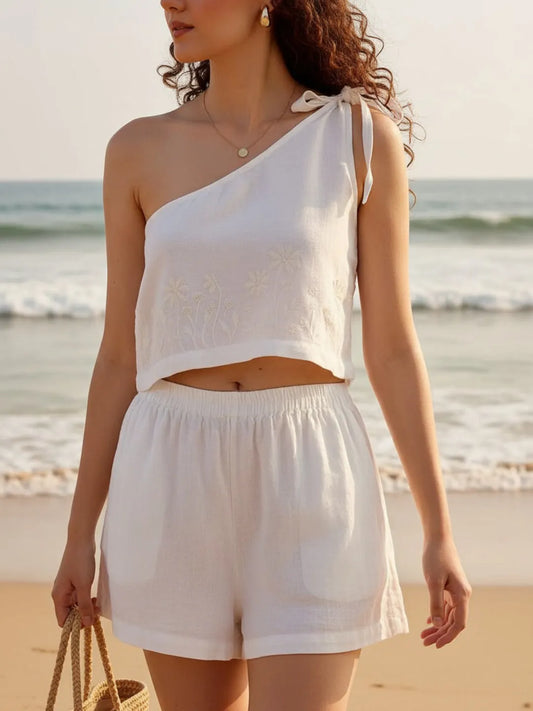 Woman in a white outfit standing on a beach with ocean waves in the background