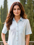 Woman in a light blue cotton linen shirt dress with embroidery standing on a balcony with greenery in the background