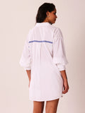 A woman shown from the back wearing a white oversized shirt dress with three-quarter puffed sleeves and a blue dotted line detail across the upper back, set against a plain light beige background.